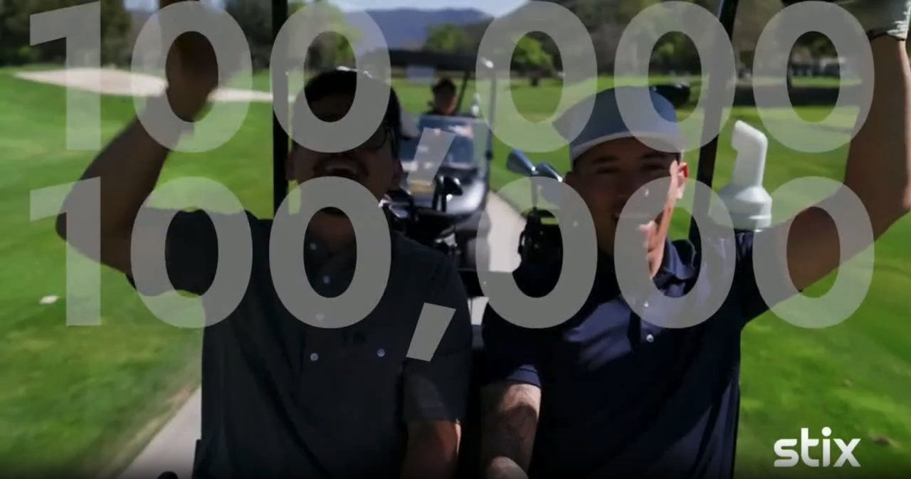 Frame from the Stix TV spot: two golfers in a cart, their faces behind a large 100,000 overlay